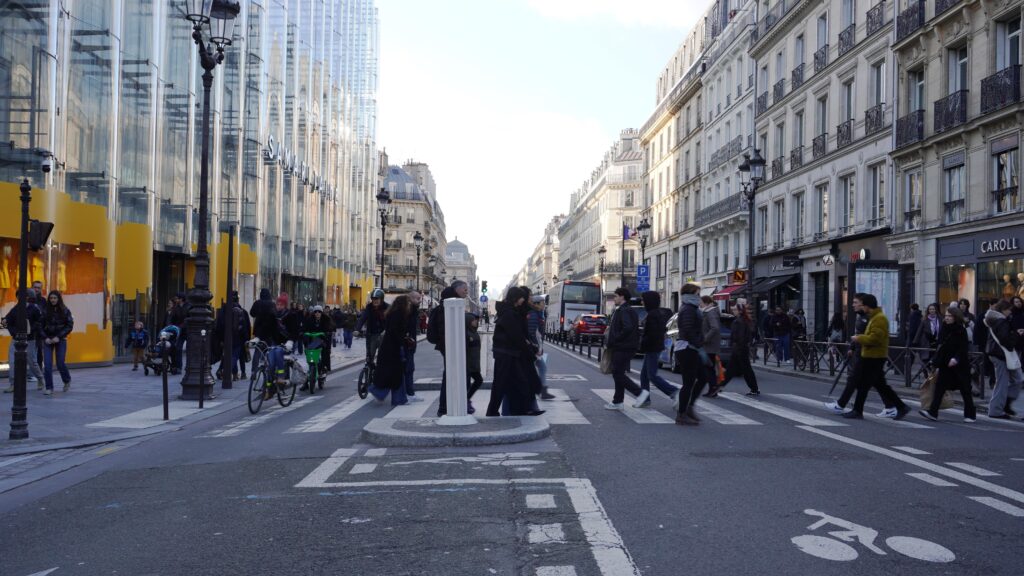 Piétons traversant la rue de Rivoli à Paris avec immeubles haussmanniens et ambiance urbaine parisienne;
